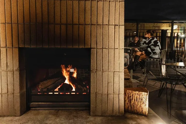 Lit outdoor brick fireplace with soldier-course brickwork on The Arborist terrace at night