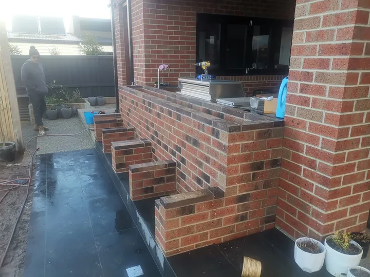 Red-brick outdoor kitchen bench with corbelled stepped detailing on a bluestone-paved patio