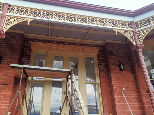 Restored red-brick Victorian porch with arched brick lintels beneath cast-iron lacework